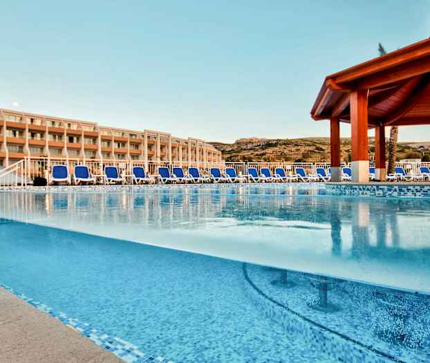 Utomhuspool med solstolar och hotellbyggnad i bakgrunden. (AI-genererad text)