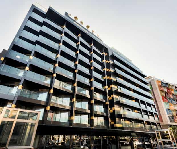 En modern byggnad med glasfasader och balkonger. Intill en annan byggnad med färgade paneler. (AI-genererad text)