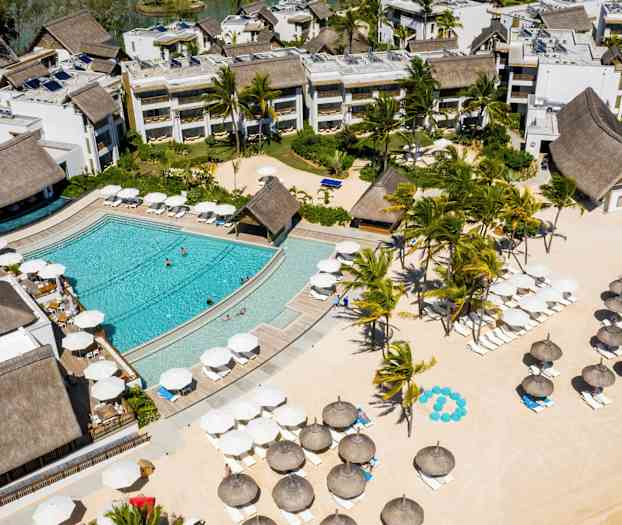 Flygvy av ett hotellområde med pool, grönska och parasoller på en sandstrand. (AI-genererad text)