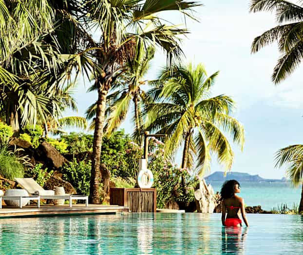En person sitter i en pool med utsikt över tropiska palmer och havslandskap. (AI-genererad text)