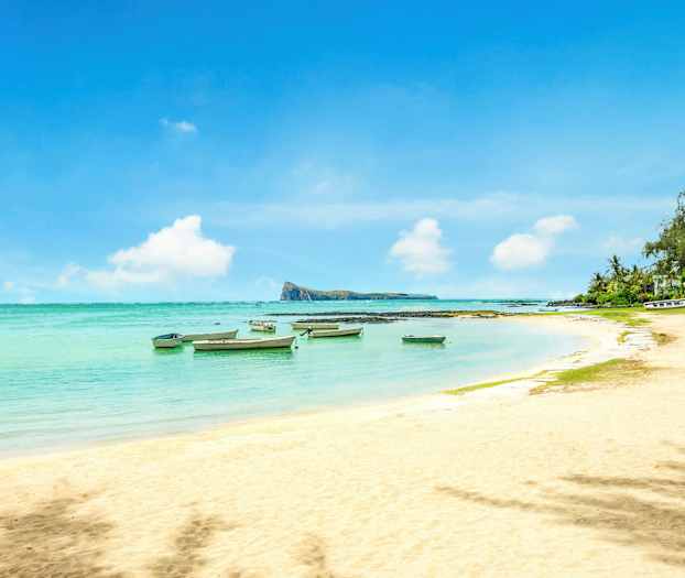 En sandstrand med småbåtar i det klara vattnet och vegetation vid kanten. (AI-genererad text)