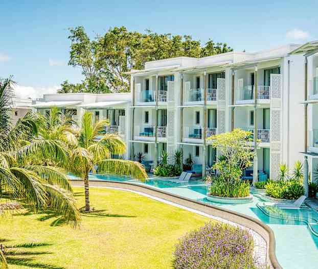 Ett modernt semesterhotell med vita byggnader och balkonger omgivna av en grönskande trädgård med tropiska växter. (AI-genererad text)