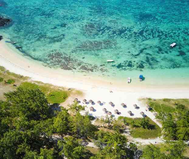 Flygbild av en tropisk strand med parasoller, båtar och omgivande grönska. (AI-genererad text)
