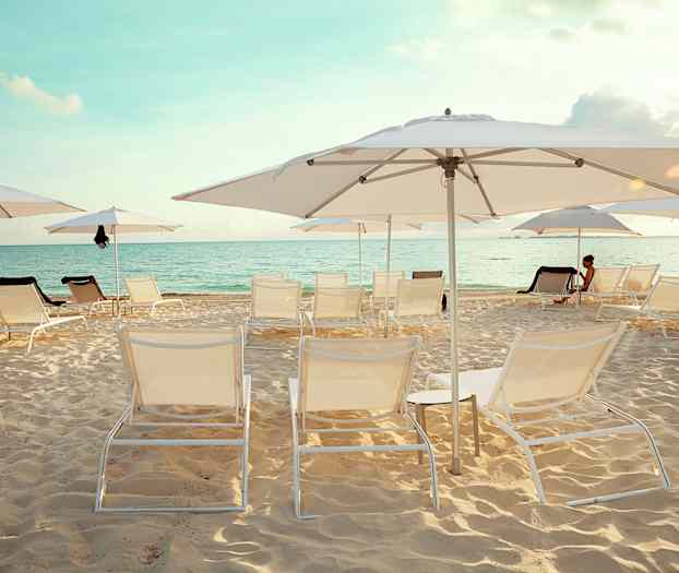 En sandstrand med solstolar och parasoller. Havet syns i bakgrunden under en klar himmel. (AI-genererad text)