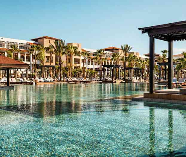 Poolområde med solsängar och byggnader i bakgrunden. (AI-genererad text)