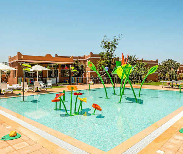 Utomhuspool med vattenlekutrustning formad som blomliknande figurer i grönt och orange, omgiven av solstolar och parasoller. (AI-genererad text)