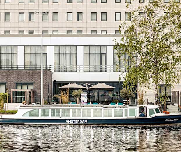 Bild av en kanalbåt framför en byggnad vid vattnet. (AI-genererad text)