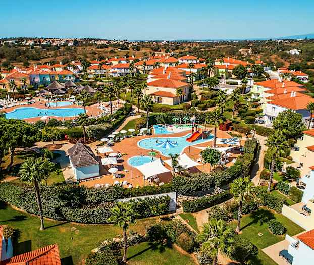 Flygfoto över ett semesterkomplex med pooler och färgglada hus. (AI-genererad text)