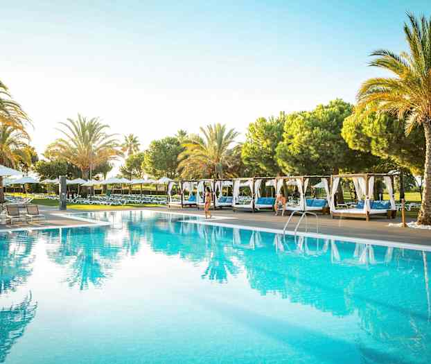 En utomhuspool omgiven av solstolar och palmer. (AI-genererad text)