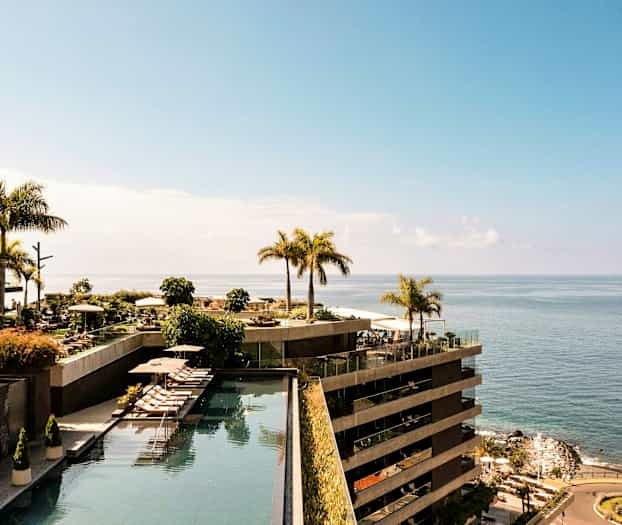 En vy över ett hotellområde vid havet, med pooler och palmer. (AI-genererad text)