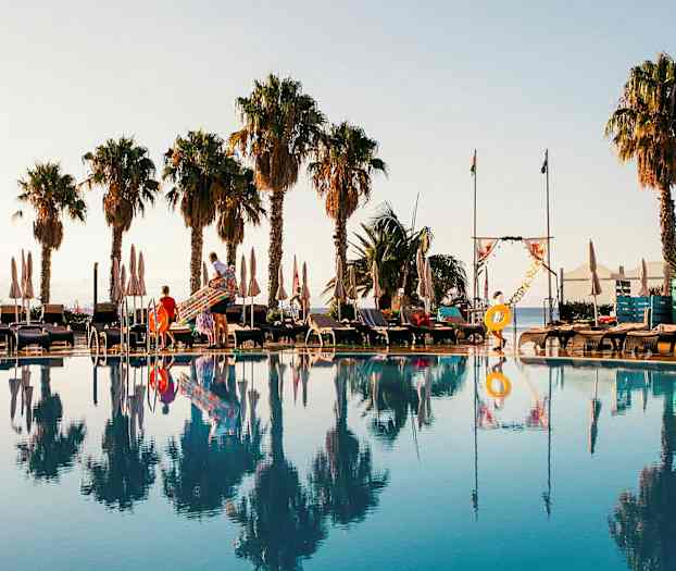 Poolområde med solstolar, parasoller och palmer i bakgrunden. (AI-genererad text)