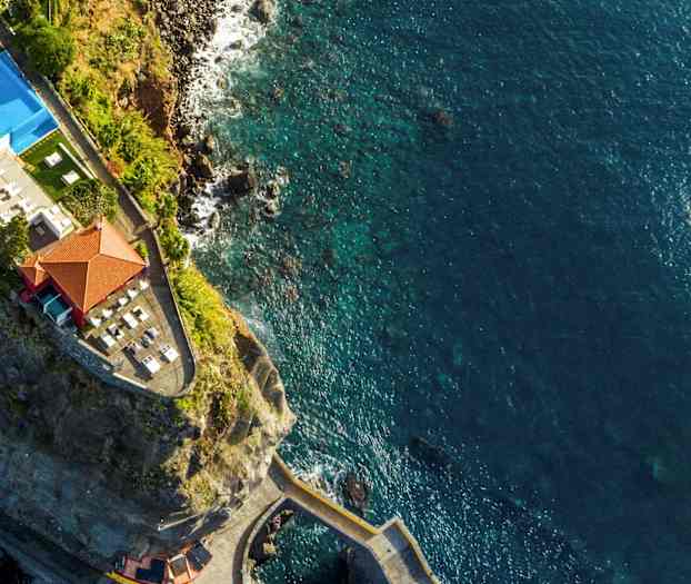 Drönarvy av en klippa med en byggnad och pool nära havet. (AI-genererad text)