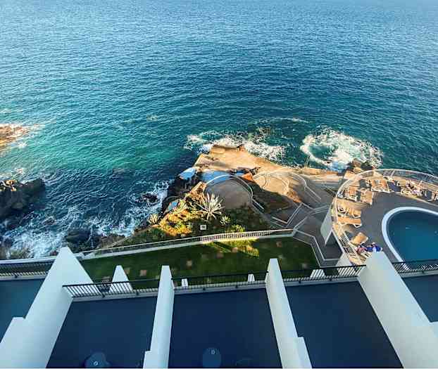 Flygbild över en anläggning vid en kust med blått hav, klippor, pool och soldäck. (AI-genererad text)