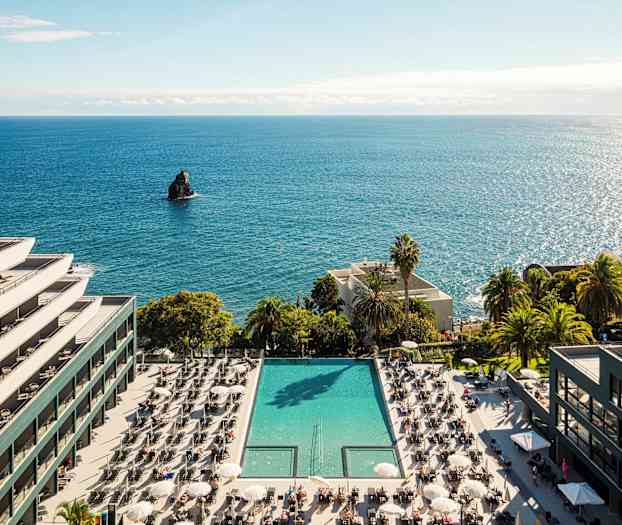 Hotell byggt vid havet med en pool och solstolar. (AI-genererad text)