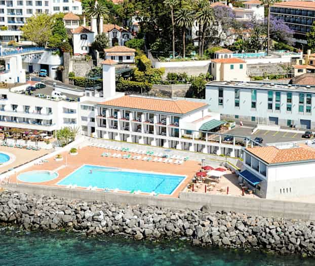 Luftfoto av ett hotell med pooler, solstolar och byggnader nära havet. (AI-genererad text)