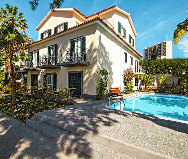 En byggnad omgiven av träd med en pool i förgrunden. (AI-genererad text)