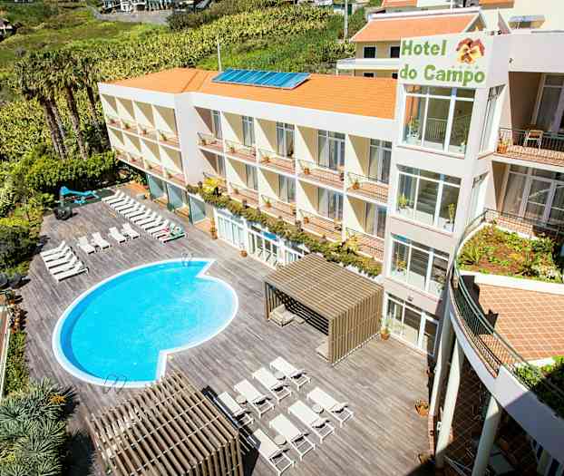 Hotellet har en utomhuspool och solstolar vid en terrass. Byggnaden har flera våningar och orange tak. (AI-genererad text)