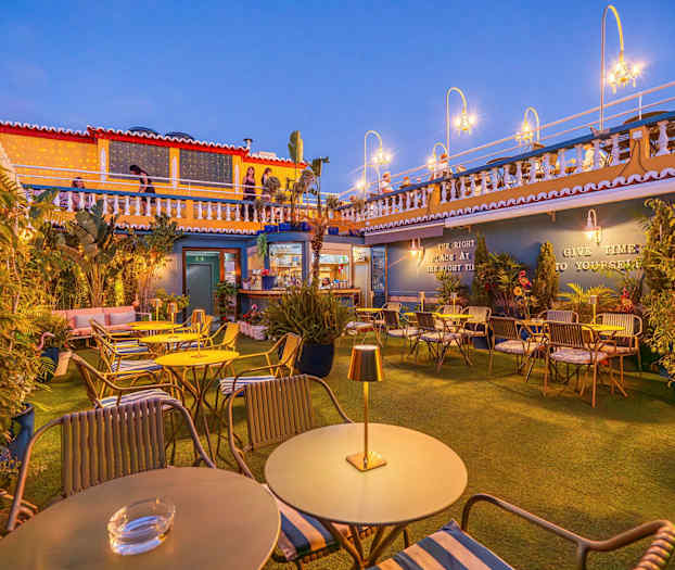 En utomhusterrass med bord och stolar, dekorerad med växter och ljuskällor. (AI-genererad text)