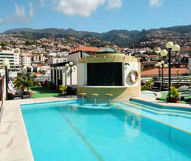 En utomhuspool på ett hotell med utsikt över staden och bergen i bakgrunden. (AI-genererad text)