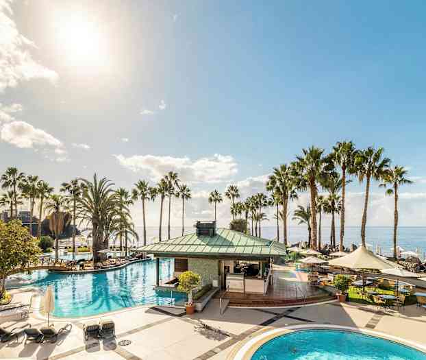 Ett poolområde med palmer och havsutsikt under en klar himmel. (AI-genererad text)