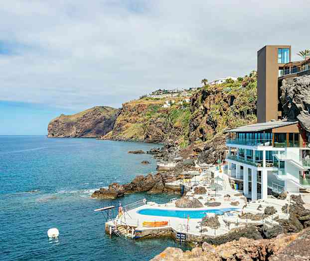 Vy över kustlandskap med hotellbyggnad och utomhuspool på en klippa vid havet. (AI-genererad text)