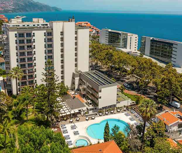 Hotellbyggnad med pool och omgivande grönska, hav i bakgrunden. (AI-genererad text)