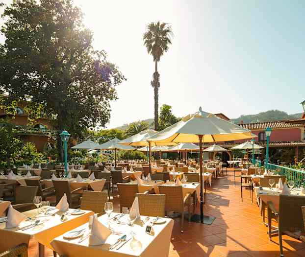 Uteservering med dukade bord, parasoller och en grönskande omgivning. (AI-genererad text)