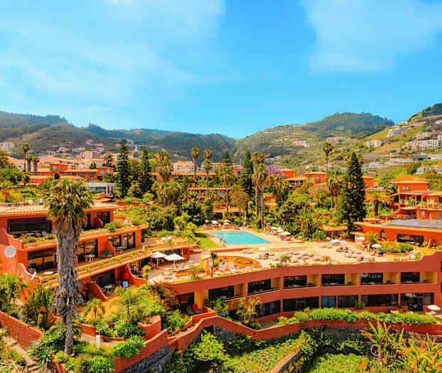 En anläggning med terrakottabyggnader, pool och grönska, belägen i en dal omgiven av kullar. (AI-genererad text)