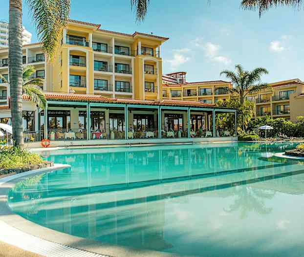 Hotellfasad vid en stor pool omgiven av palmer. (AI-genererad text)