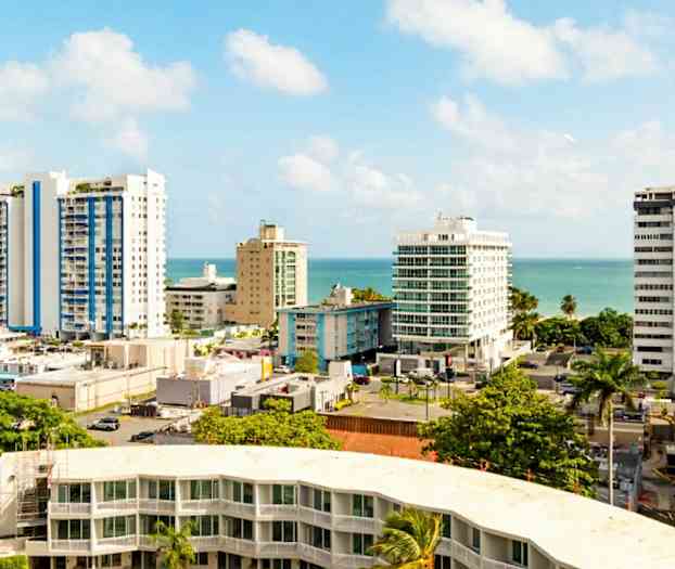 Stadsvy med höghus och palmer nära havet under en klarblå himmel. (AI-genererad text)