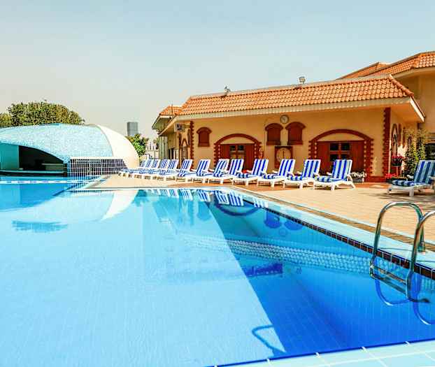 En pool vid ett hotell med solstolar och en bar i bakgrunden. (AI-genererad text)