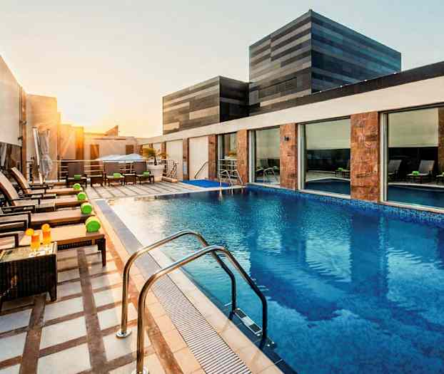 En modern pool på en byggnadsterrass med solstolar och bord, omgiven av glas och stenpaneler. (AI-genererad text)