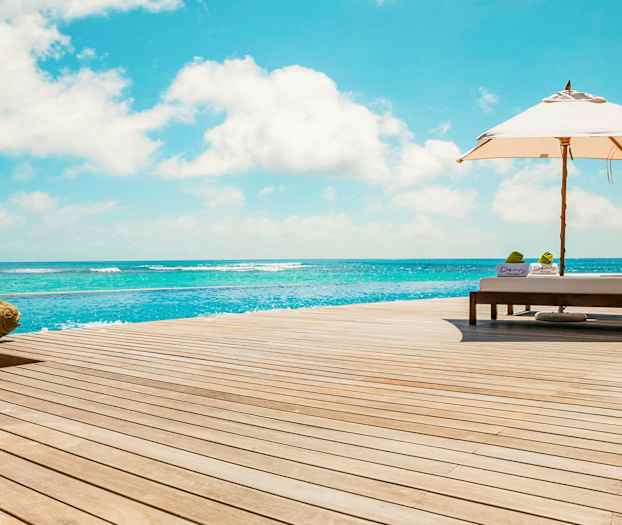 Solstolar och parasoll vid ett trädäck intill havet. (AI-genererad text)