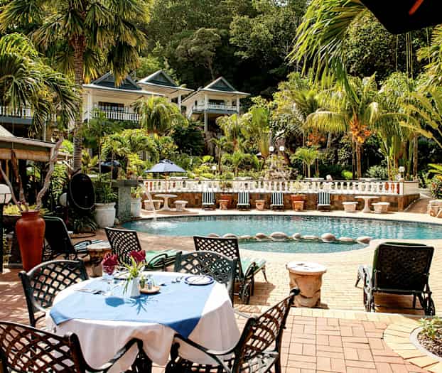 En utomhuspool omgiven av palmer och grönska med en möblerad sittgrupp nära vattnet. (AI-genererad text)