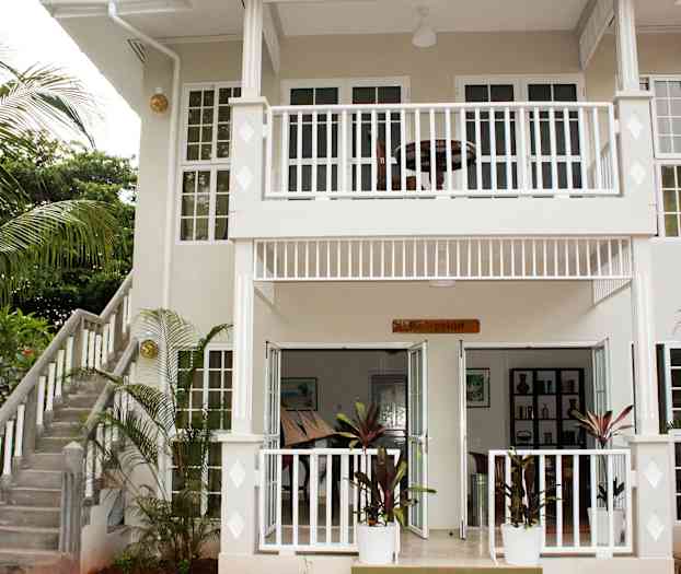 Entrén till en tvåvåningsbyggnad med ett skylt vid ingången där det står "Reception" och en omgivande trädgård. (AI-genererad text)