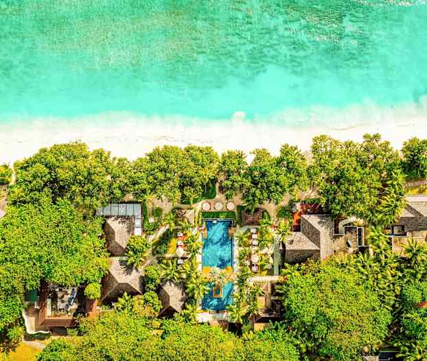 Flygbild över ett hotell vid en strand med pool, som omges av grönska. (AI-genererad text)