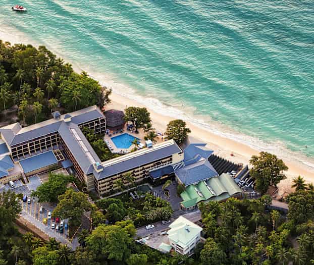 Flygfoto av hotell med tillhörande poolområde vid stranden. (AI-genererad text)