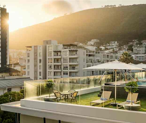 Takterrass med solstolar, bord och parasoller, pool i bakgrund samt en stadsmiljö med grönskande kullar. (AI-genererad text)