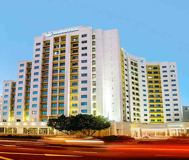 Ett modernt hotell med en hög byggnad och många fönster ligger intill en trafikerad gata på kvällen. (AI-genererad text)