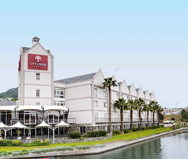 Ett hotell med ljus fasad, kantat av palmer och en kanal framför. (AI-genererad text)