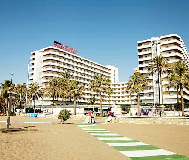 En strandpromenad framför höga lägenhetsbyggnader med palmträd i förgrunden. (AI-genererad text)