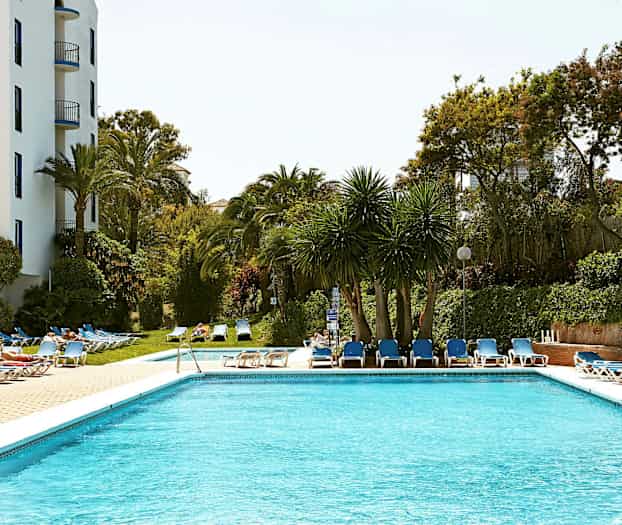 En pool omgiven av solstolar och träd. (AI-genererad text)