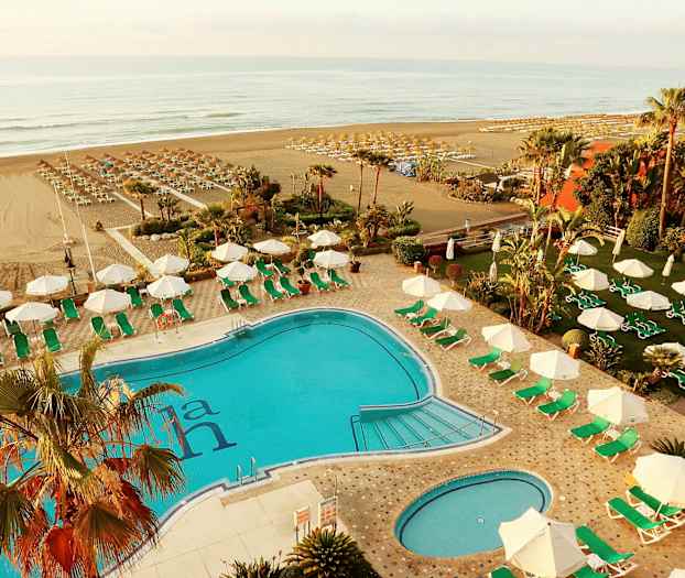 En utomhus pool med omgivande solstolar och parasoller, strand synlig i bakgrunden. (AI-genererad text)