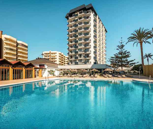 Hotellbyggnad med pool i förgrunden. (AI-genererad text)