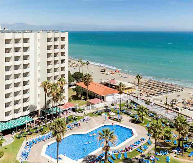 Ett hotell med pool och solstolar nära en sandstrand vid havet. (AI-genererad text)