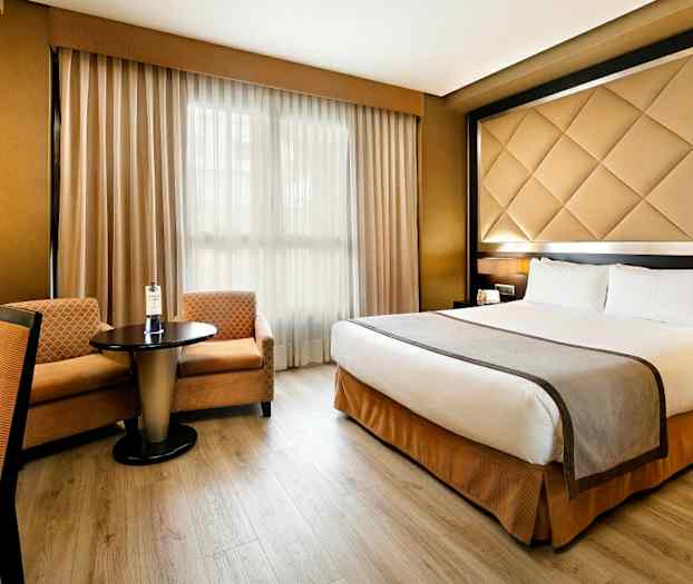 Ett hotellrum med en dubbelsäng, ett bord med två stolar och fönster med gardiner. (AI-genererad text)