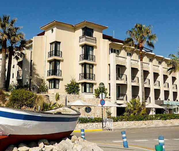 En byggnad med balkonger och palmer framför, samt en båt på land. (AI-genererad text)