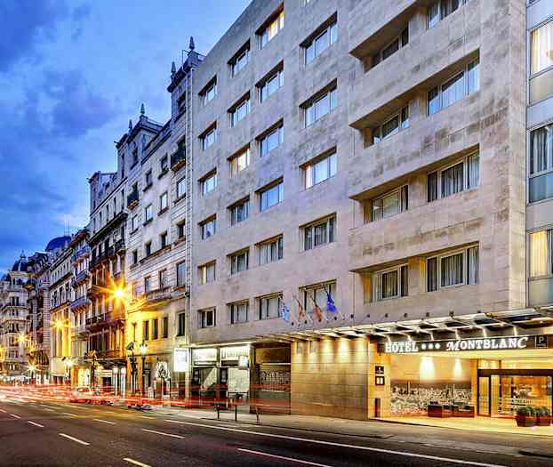 En stadsgata med ett hotell som heter Montblanc syns på högra sidan, med flerfasadiga byggnader och kvällsbelysning. (AI-genererad text)