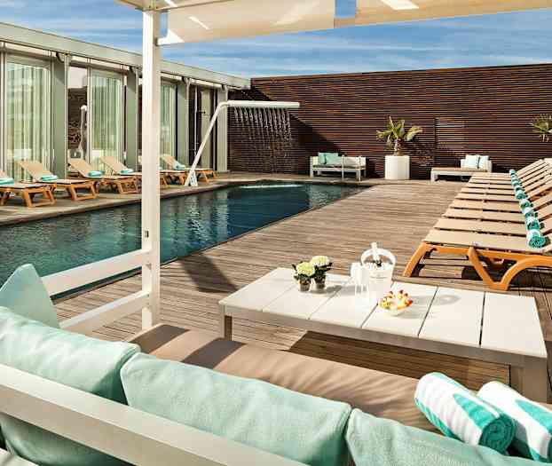 En utomhuspool med solstolar och handdukar på ett trädeck, samt ett bord med dekorationer och parasoll. (AI-genererad text)