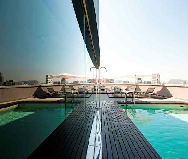 En takpool med träplattformar och solsängar bredvid. Staden syns i bakgrunden. (AI-genererad text)